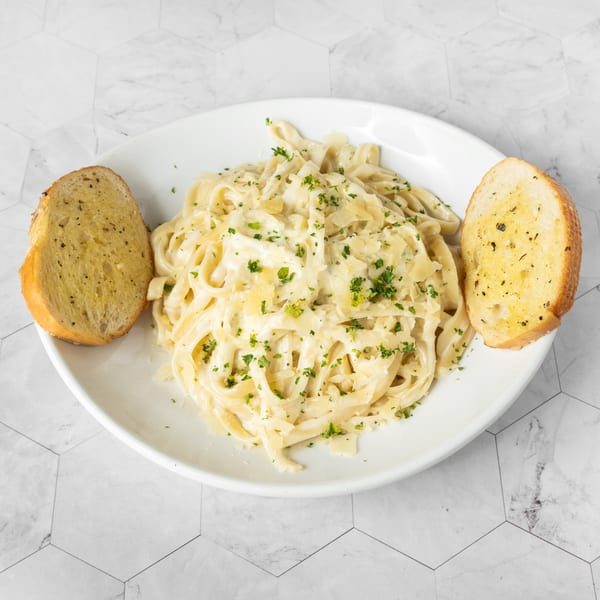 Creamy fettuccine alfredo pasta with parmesan, parsley, and two slices of garlic bread on a white plate.