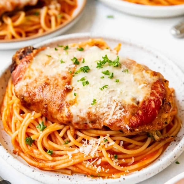 Chicken parmesan with melted cheese and red sauce, served over spaghetti on a white plate.