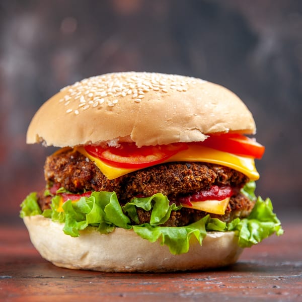 Close-up of a double cheeseburger with lettuce, tomato, and ketchup on a sesame seed bun.